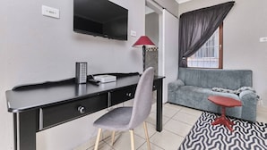 A modern room with a desk, chair, TV, sofa, and a small table. - The Cozy 1 Bedroom Apartment (Johannesburg)