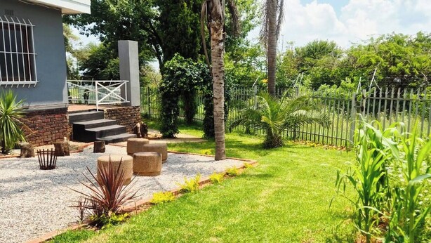 A residential property with a paved driveway, a stone bench, a small garden with a palm tree, and a metal fence. - The Cozy 1 Bedroom Apartment (Johannesburg)