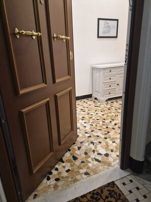 Ein Zimmer mit Holztür, Fliesenboden, weißem Schminktisch und einem gerahmten Bild an der Wand.