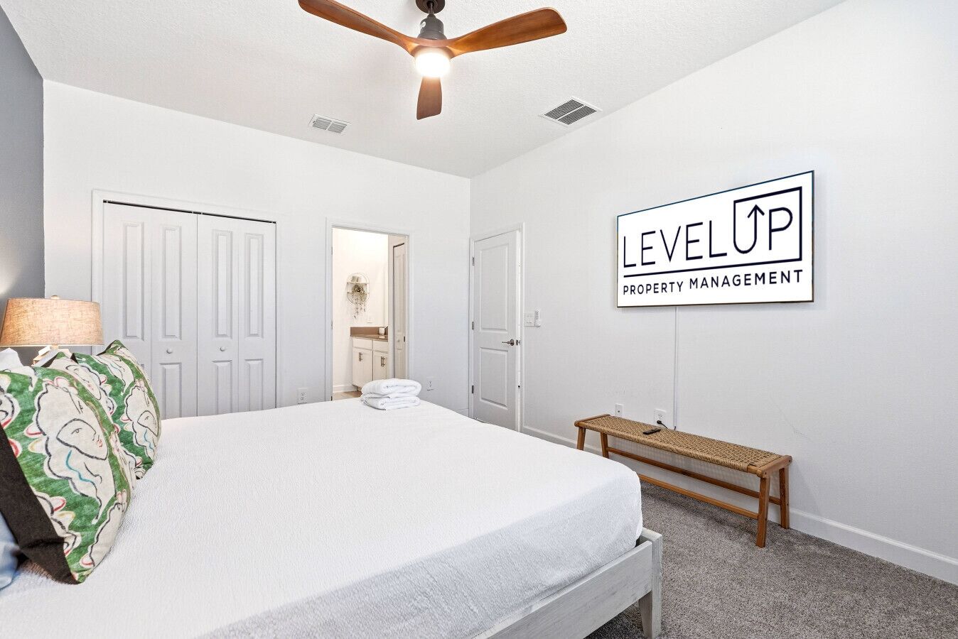 A bedroom with a bed, a ceiling fan, a bench, and a wall sign.