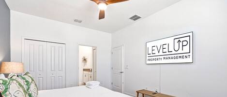 A bedroom with a bed, a ceiling fan, a bench, and a wall sign.