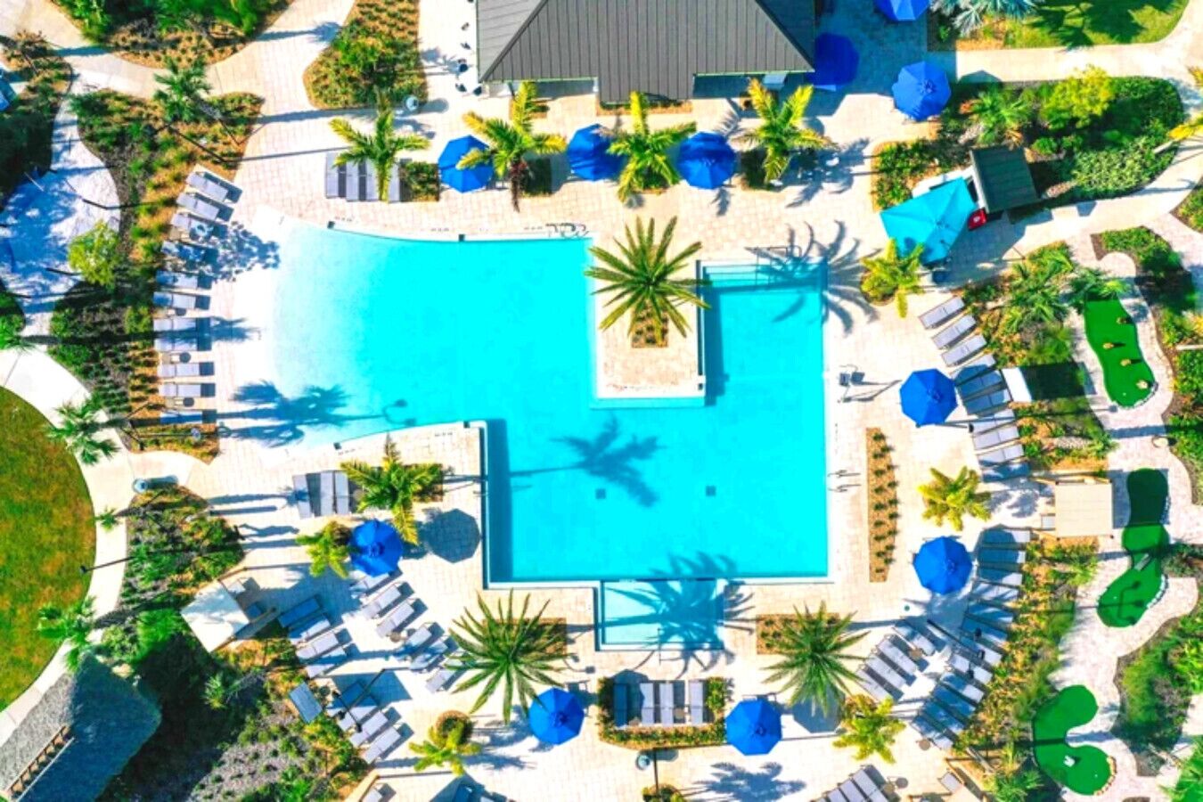 Vista aérea de um resort com piscina central, espreguiçadeiras e palmeiras.