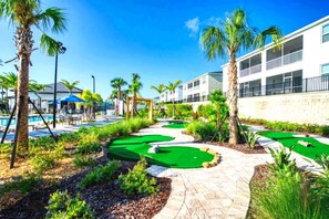 Een golfbaan met een zwembad, palmbomen en een gebouw met balkons.