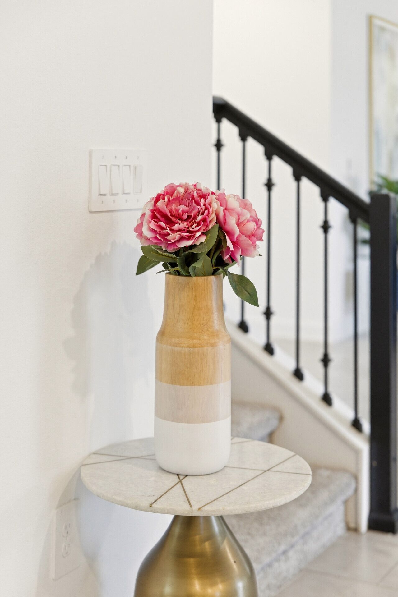 A vase with flowers on a table near a staircase.