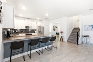 A modern kitchen with a central island, bar stools, stainless steel appliances, and a staircase leading to another level. - Resort included~Heated Pool~Game Room~Near Disney (Davenport)