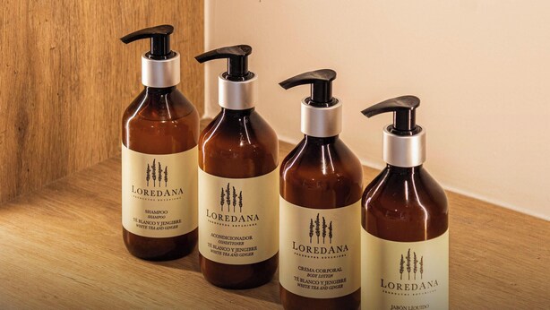 Cuatro botellas de productos Loredana sobre una superficie de madera.