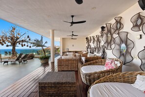 Ein sonniger Außenbereich mit Lounge-Möbeln aus Rattangeflecht, Deckenventilatoren und dekorativer Wandgestaltung.