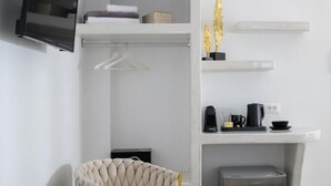 Ein modernes Zimmer mit einer Couch, einem kleinen runden Tisch, einem an der Wand befestigten Fernseher, einem Mini-Kühlschrank und einer Kaffeemaschine auf einem Regal.