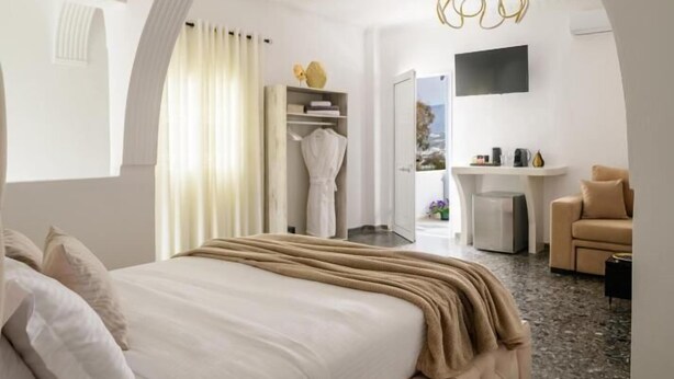 Ein modernes Hotelzimmer mit einem großen Bett, einer Sitzecke, einem Schreibtisch und Blick durch eine gewölbte Tür.