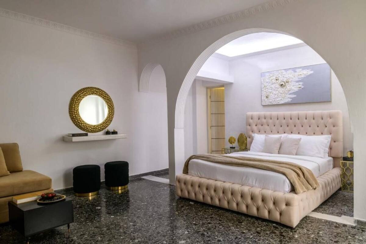 Un dormitorio con una cama capitonada, un espejo redondo, un sofá y una mesa de centro.