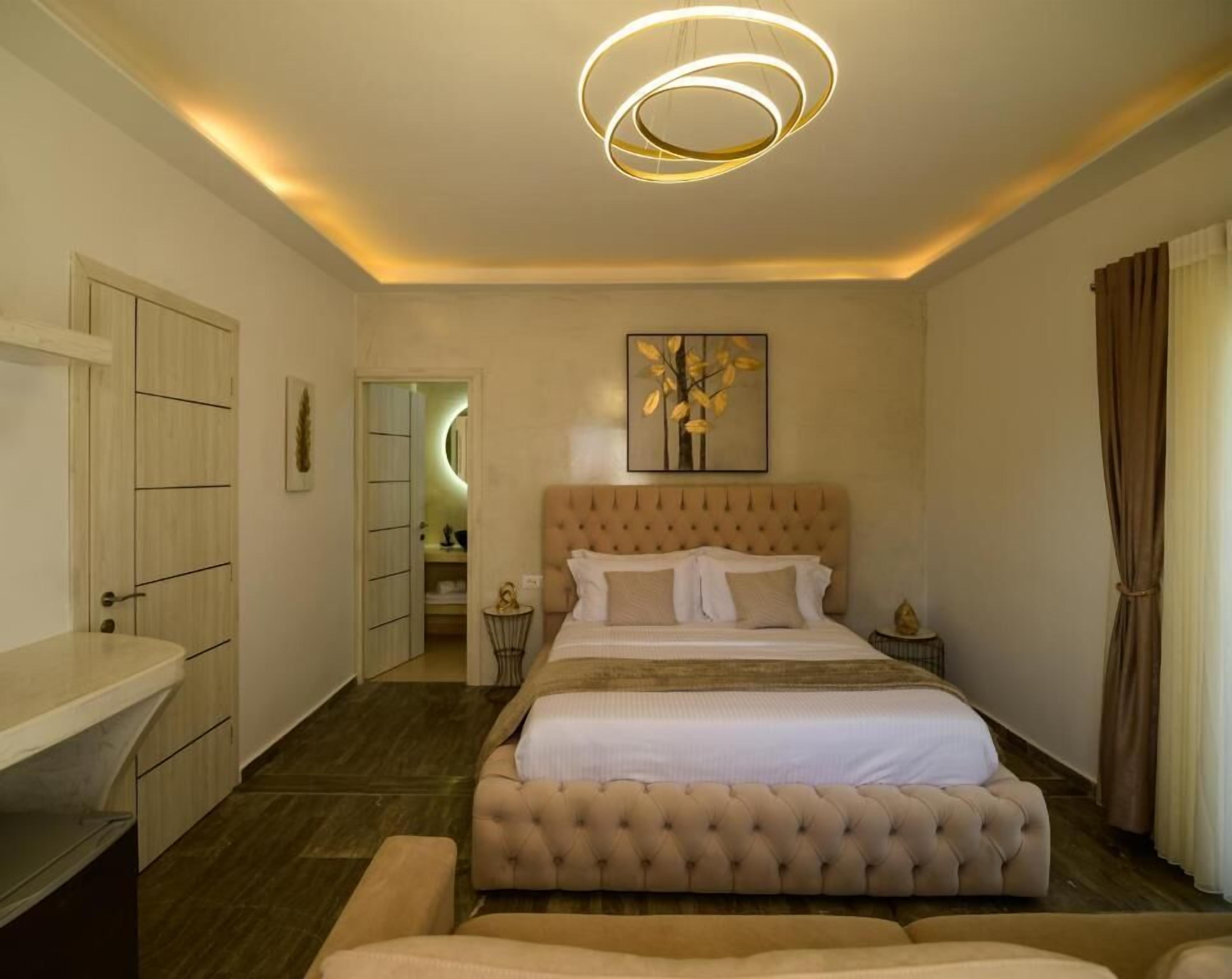A bedroom with a tufted headboard bed, a bedside table, a mirror, and a ceiling light fixture.