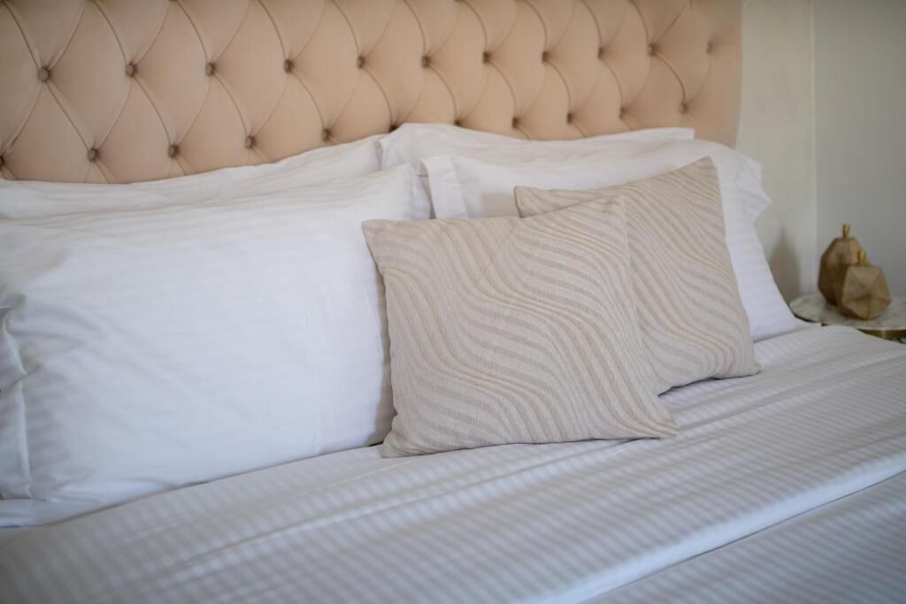 Una cama con cabecera acolchada, ropa de cama blanca y dos almohadas.