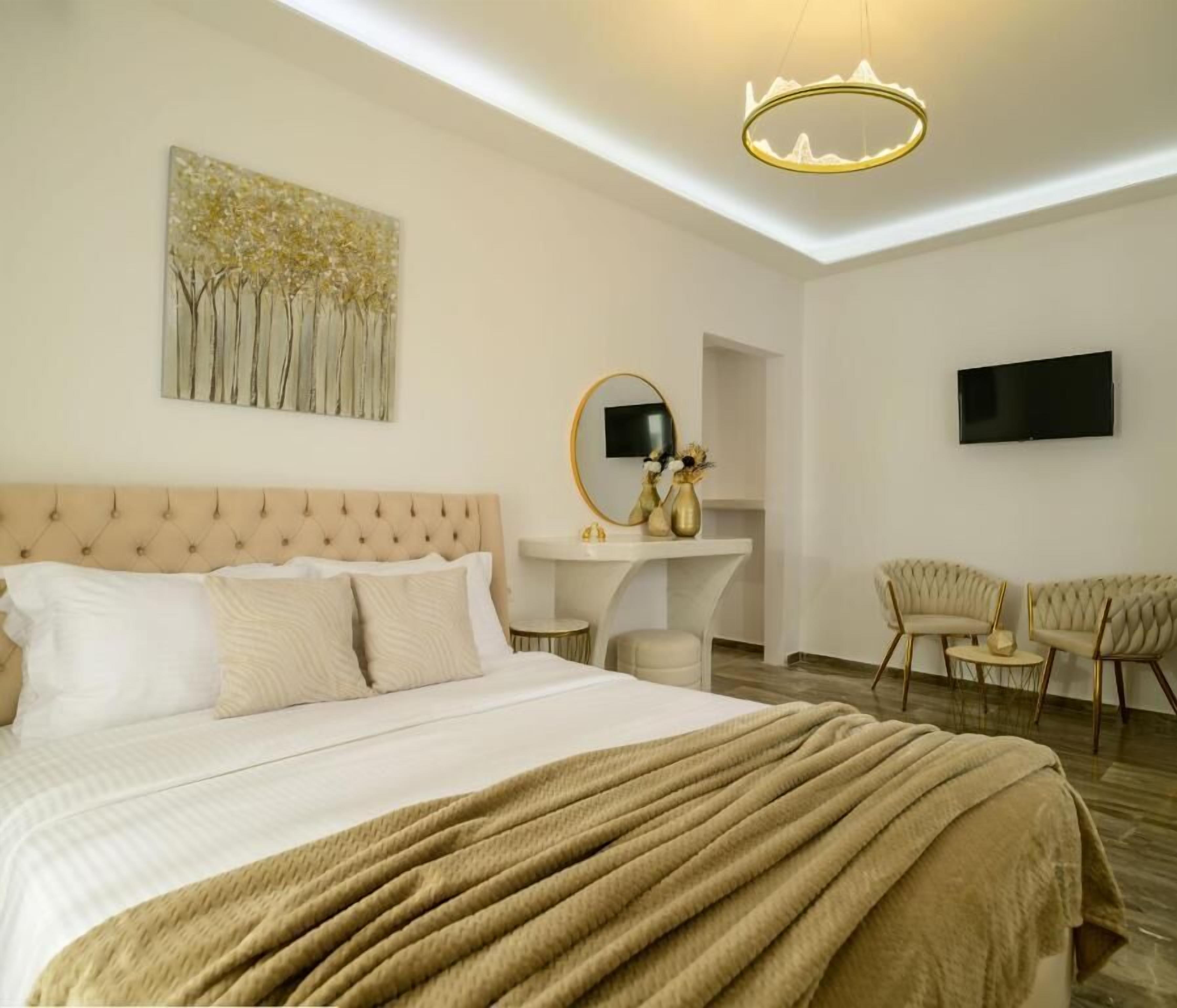 A bedroom with a bed, a bedside table, a mirror, a TV, and a seating area with two chairs.