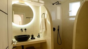 Ein Badezimmer mit rundem Spiegel, einem schwarzen Waschbecken, einem Handtuch, einer Handbrause und einem wandmontierten Wasserhahn.