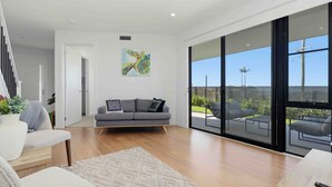 A modern living room with a grey sofa, a patterned rug, and a large sliding glass door leading to an outdoor patio. - Panoramic Point by Experience Jervis Bay (Vincentia)
