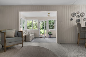 A room with a sofa, a chair, a rug, a dining table, and a view through a glass door.