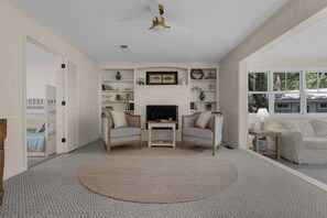 A living room with a fireplace, two armchairs, a coffee table, and a TV.