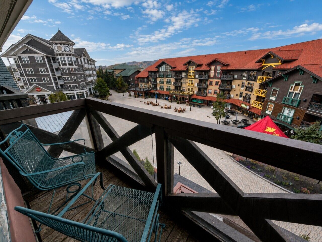 Een balkon met metalen stoelen en uitzicht op een hotel met meerdere gebouwen en balkons.
