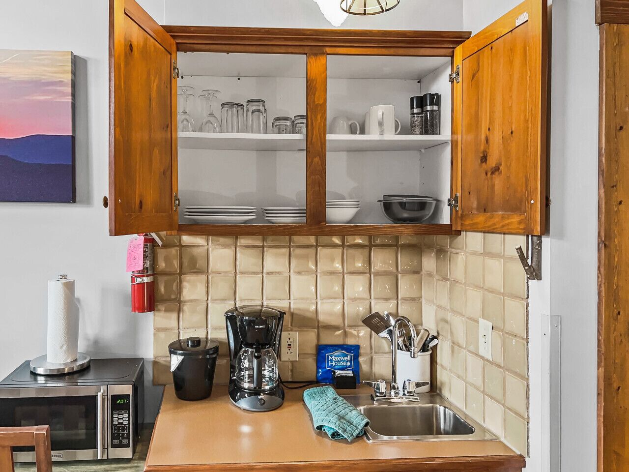 Une cuisine avec des meubles de rangement en bois, une machine à café, un four à micro-ondes et un dosseret carrelé.