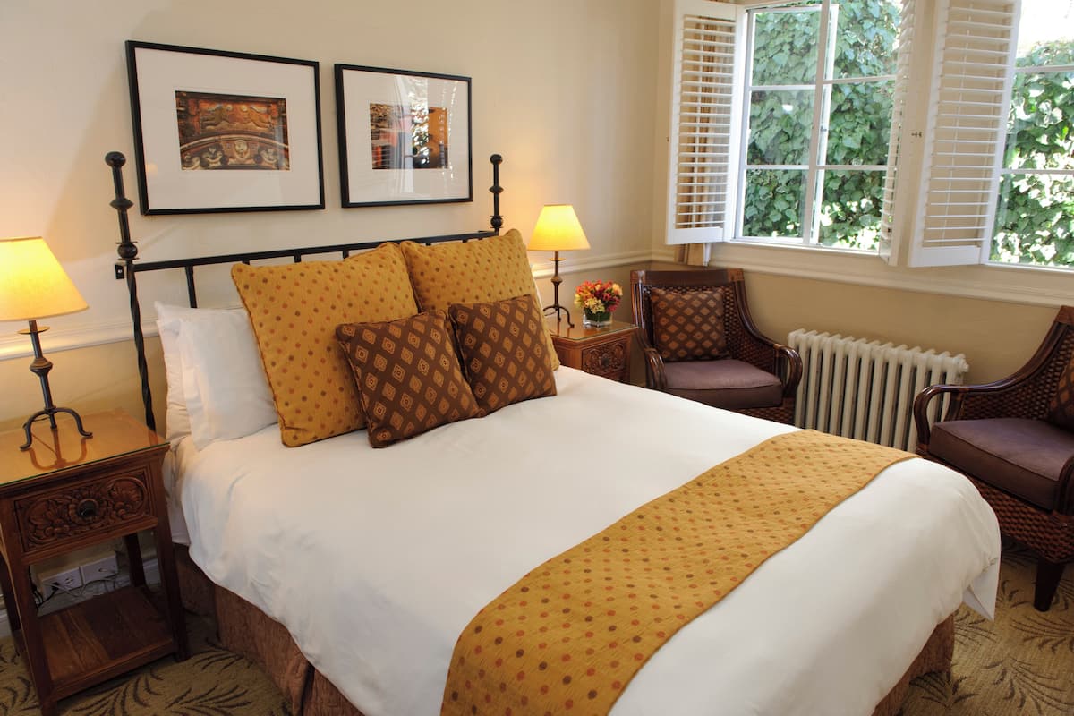 A neatly made bed with patterned pillows, a bedside table with a lamp, a chair, and framed pictures on the wall.