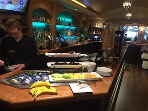 Angolo bar con un bancone che espone diversi cibi, un barista e una vetrina piena di bottiglie.