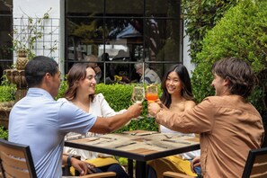 A group of people toasting at a table with a view of a building and greenery in the background.