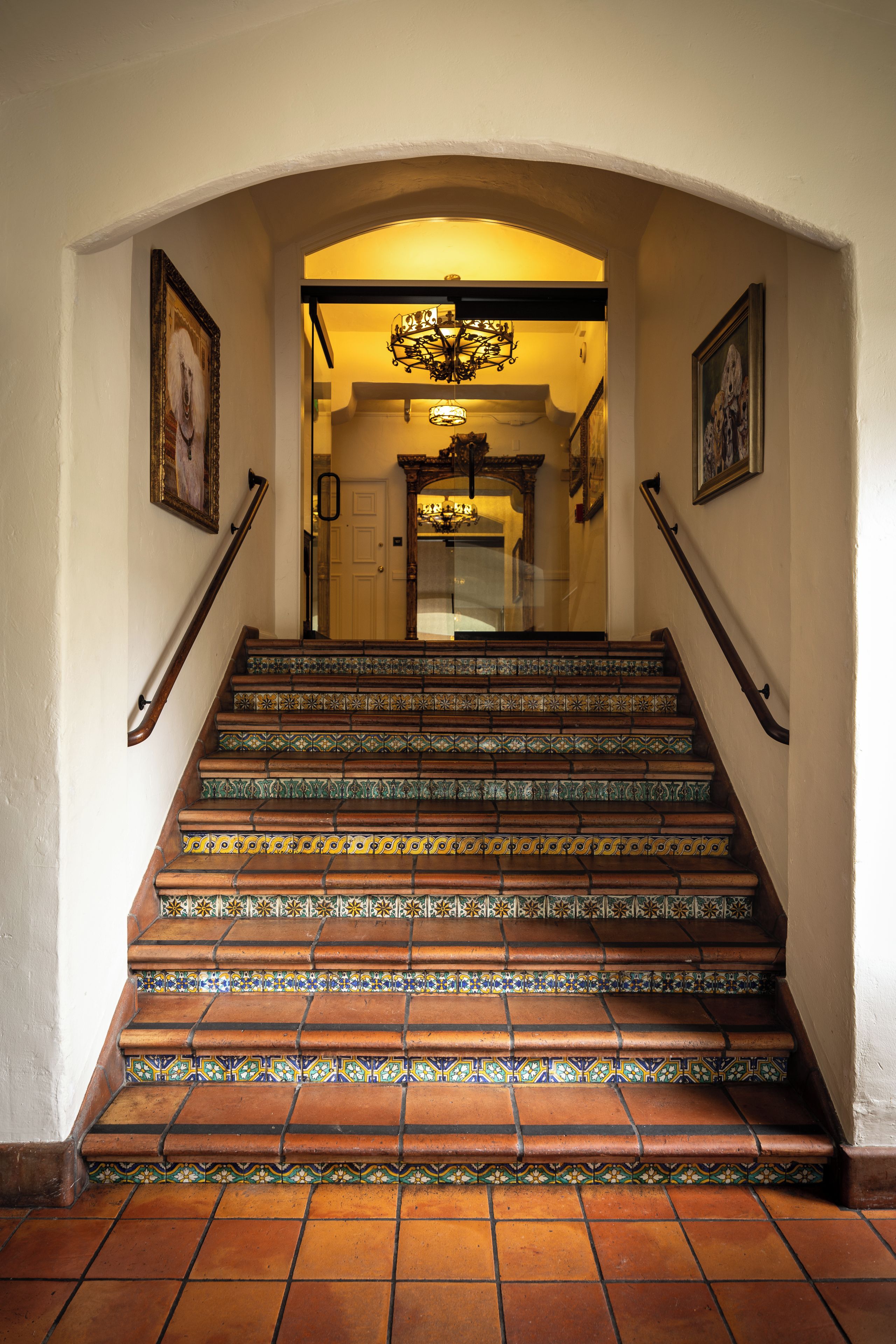 Una escalera con barandillas decorativas y baldosas estampadas que conduce a una habitación con candelabro.