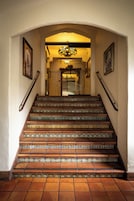 Una escalera con barandillas decorativas y baldosas estampadas que conduce a una habitación con candelabro.