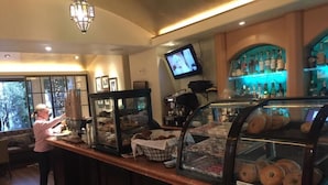 Uma área de bar com balcão, uma tela de televisão e uma vitrine com doces.