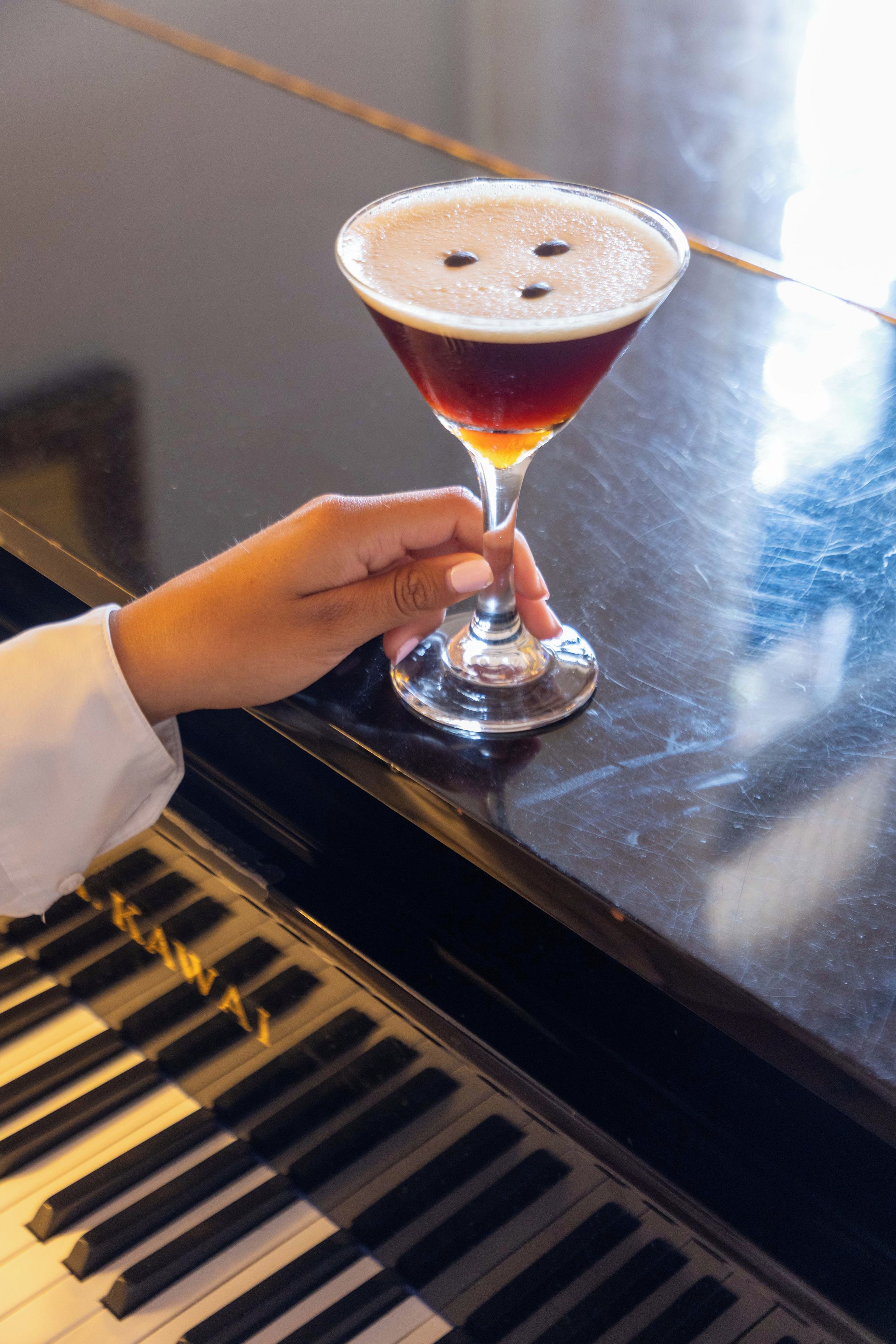 A hand holding a martini glass on a piano.
