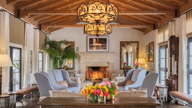 Um quarto amplo com uma grande mesa de jantar de madeira, duas poltronas, uma lareira e um candelabro.