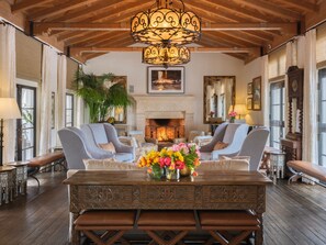 A spacious room with a large wooden dining table, two armchairs, a fireplace, and a chandelier. - Cypress Inn (Carmel)