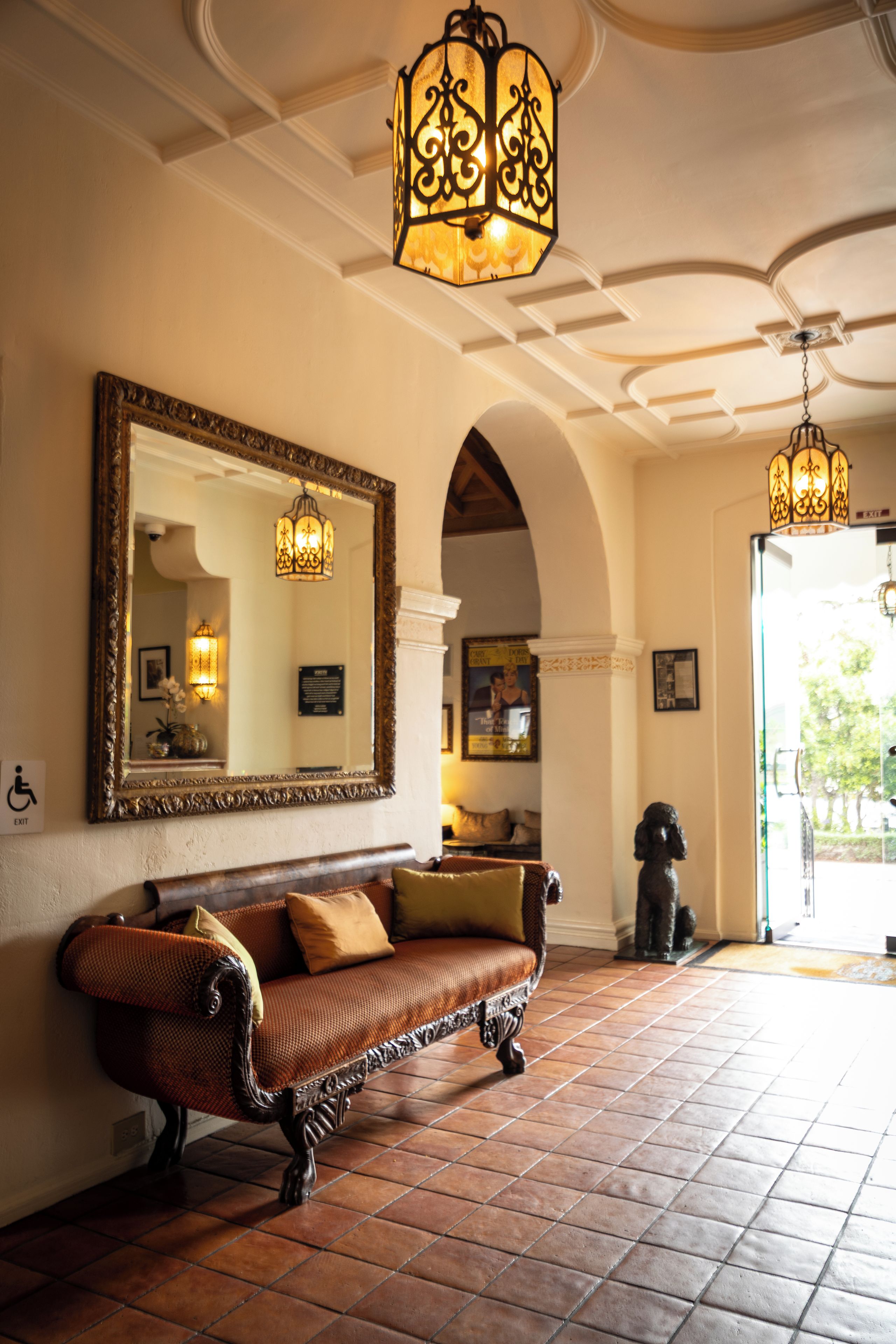 A lobby with a large ornate mirror, a vintage sofa, and a tiled floor.