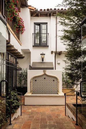 Un patio con una pared de azulejos, un balcón con flores y una escalera que lleva a una puerta.