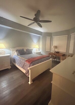 Ein Schlafzimmer mit einem Bett, zwei Nachttischlampen, einem Deckenventilator, einem Nachttisch, einem Stuhl und einer Kommode.