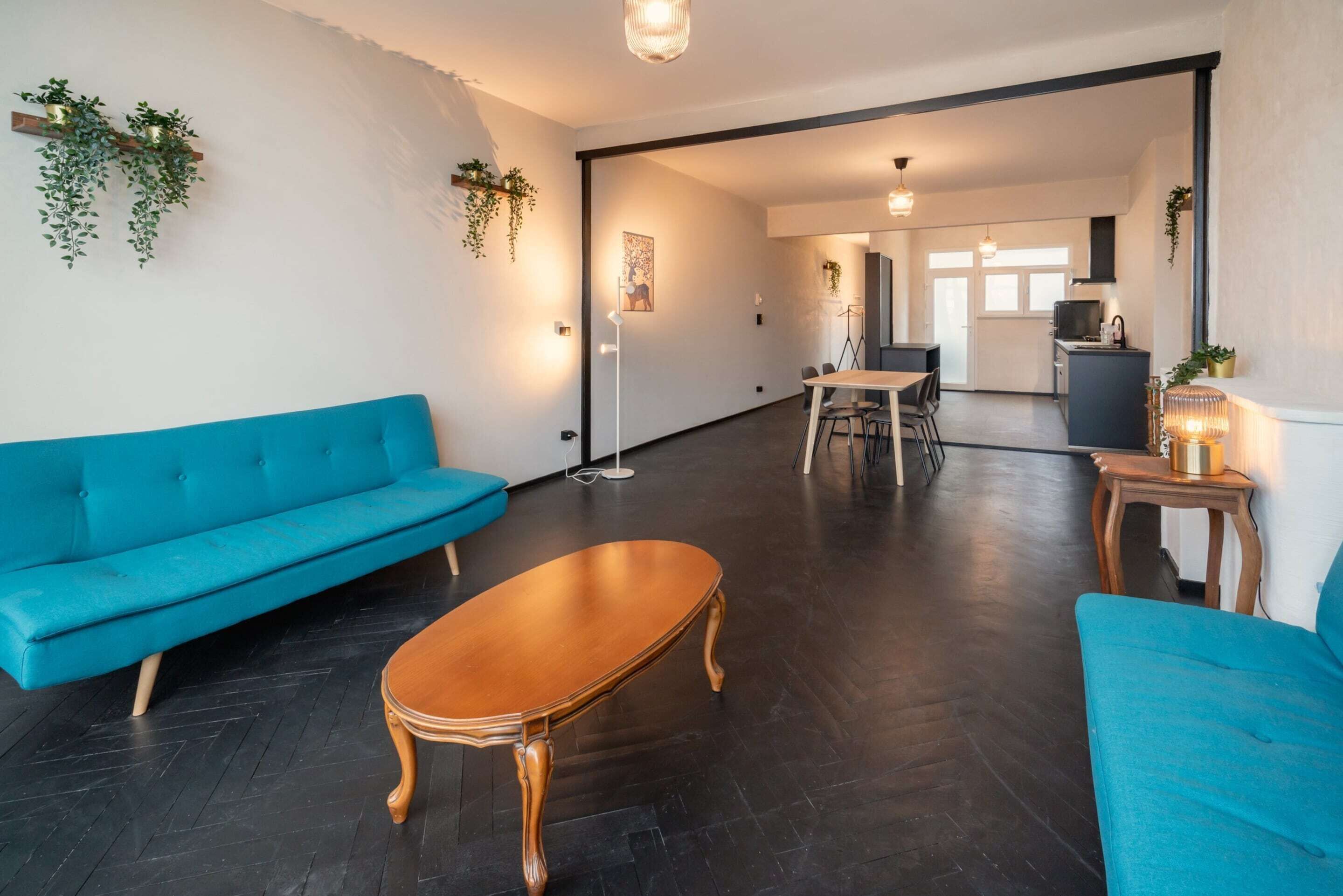 A modern living room with a blue sofa, a wooden coffee table, and a dining area with a table and chairs.