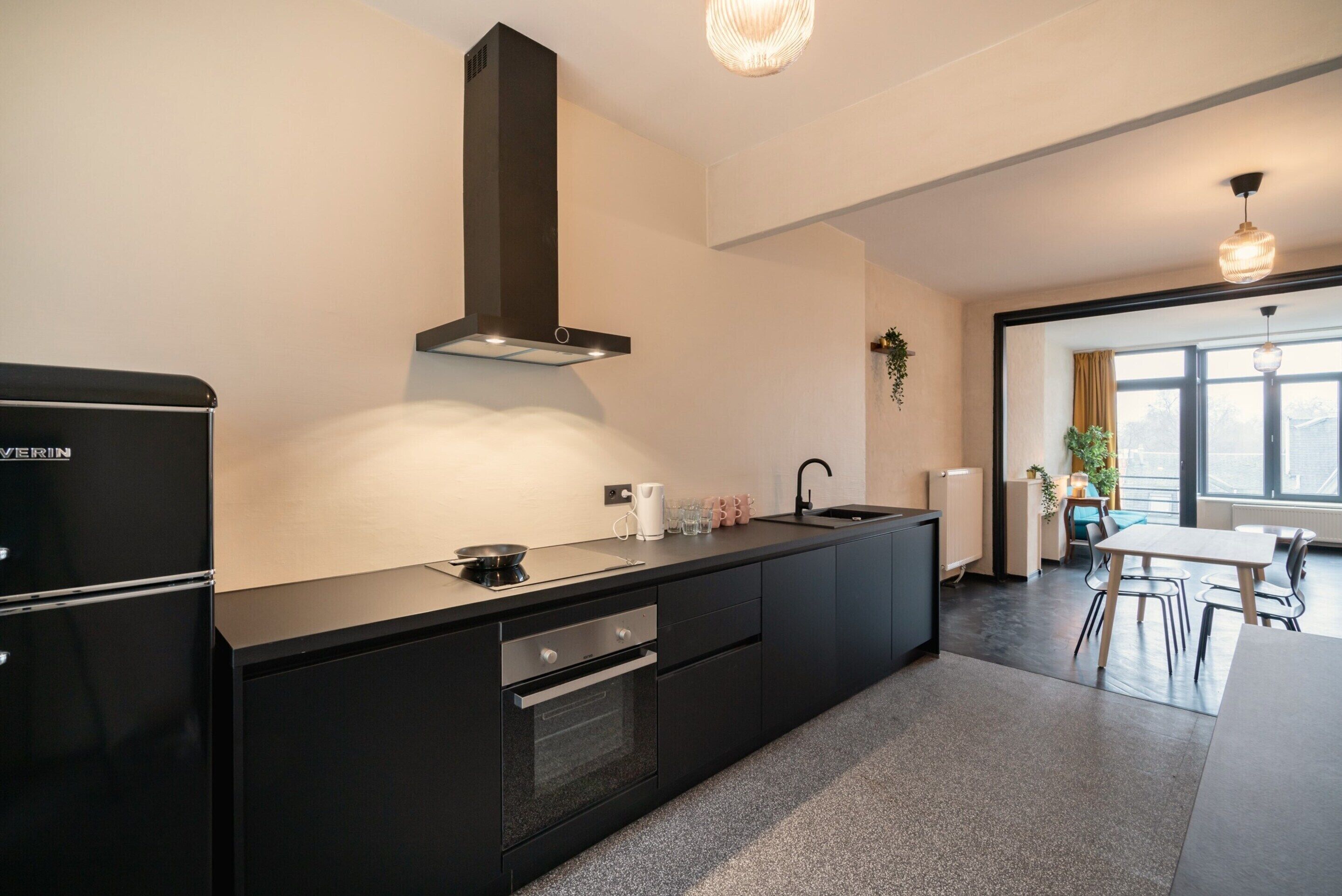 Una cocina moderna con un refrigerador, horno y pileta negros, un extractor de aire negro y una zona de comedor con mesa y sillas.