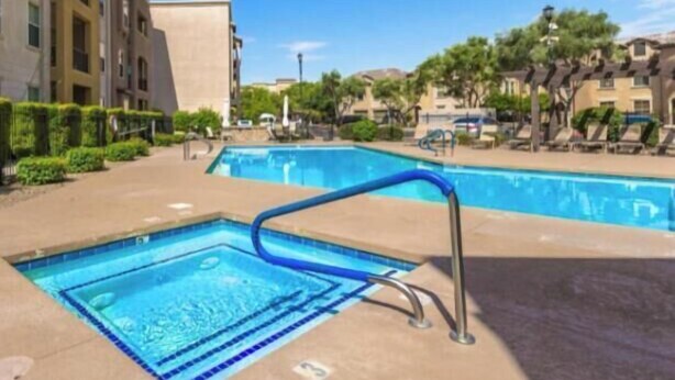Una piscina con una escalera metálica, rodeada de una zona pavimentada y edificios.