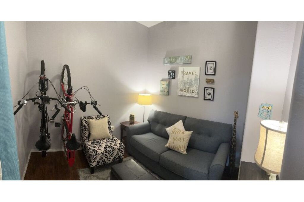 Un salon avec un canapé gris, un fauteuil à motifs et un vélo rouge.
