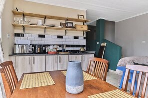 Una cocina con estantes de madera, una mesa de comedor con sillas y un florero.