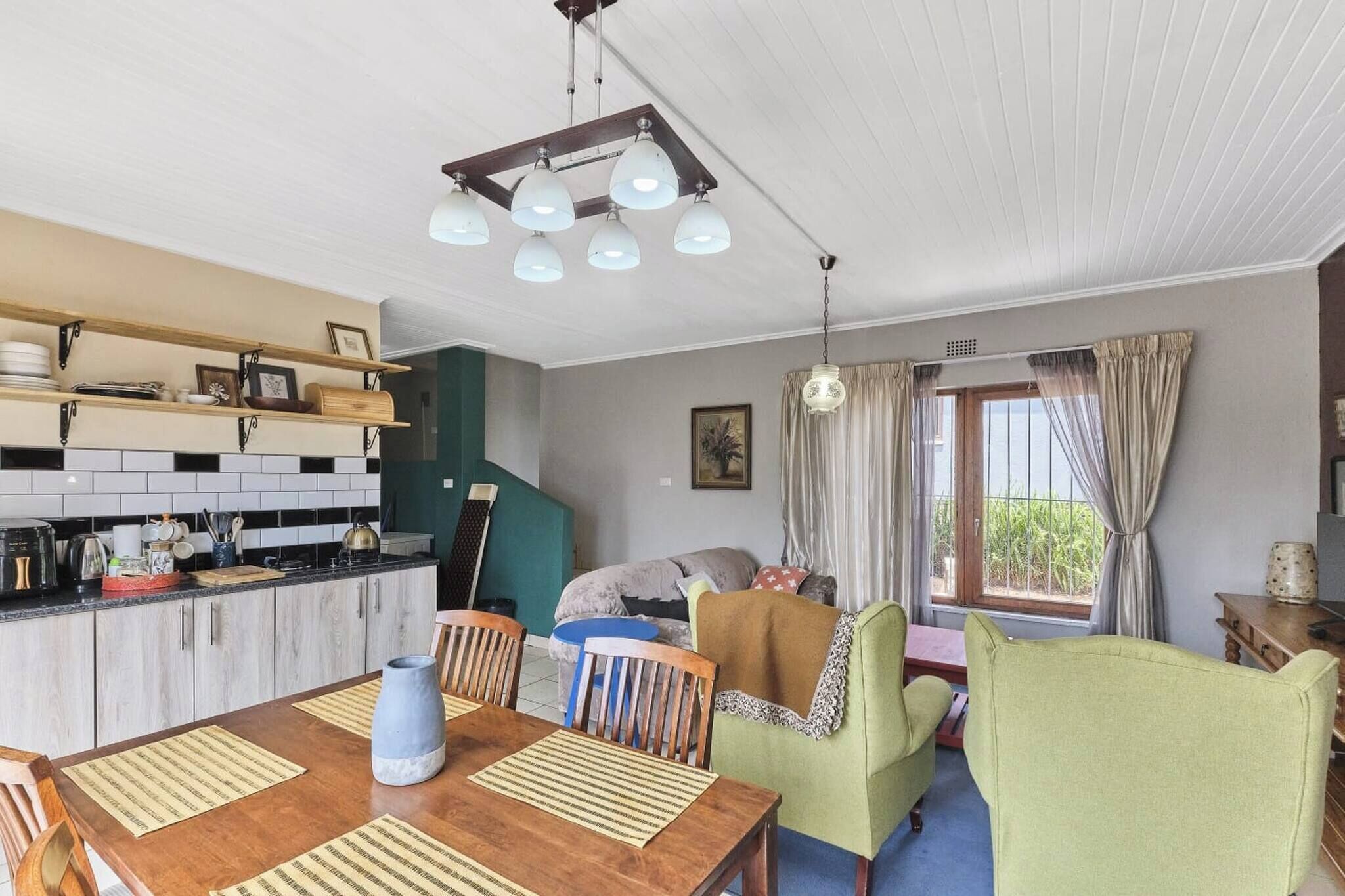 Ett kompakt bostadsutrymme med ett kök, en matplats och ett fönster med gardiner.