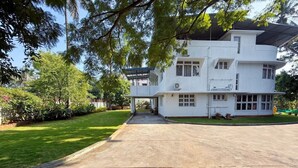 A multi-story white building with a flat roof, a covered driveway, and a well-maintained lawn. - Himalaya 6BHK bungalow with AC in Mysuru (Mysuru)