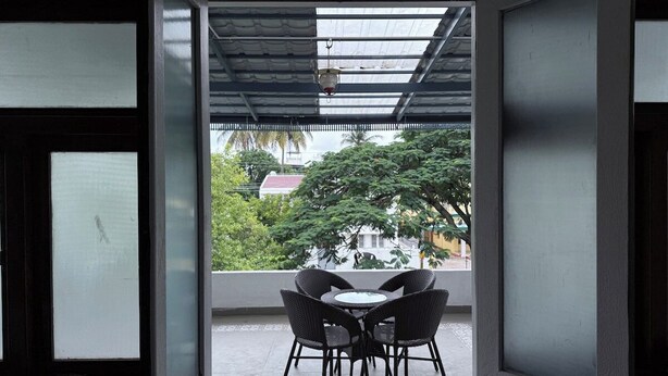 An open doorway leading to a balcony with a table and chairs, a hanging light fixture, and a view of greenery and buildings. - Himalaya 6BHK bungalow with AC in Mysuru (Mysuru)