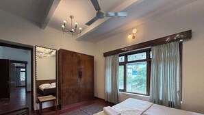 A bedroom with a bed, a wardrobe, a desk, a chair, a ceiling fan, and a window with curtains. - Himalaya 6BHK bungalow with AC in Mysuru (Mysuru)