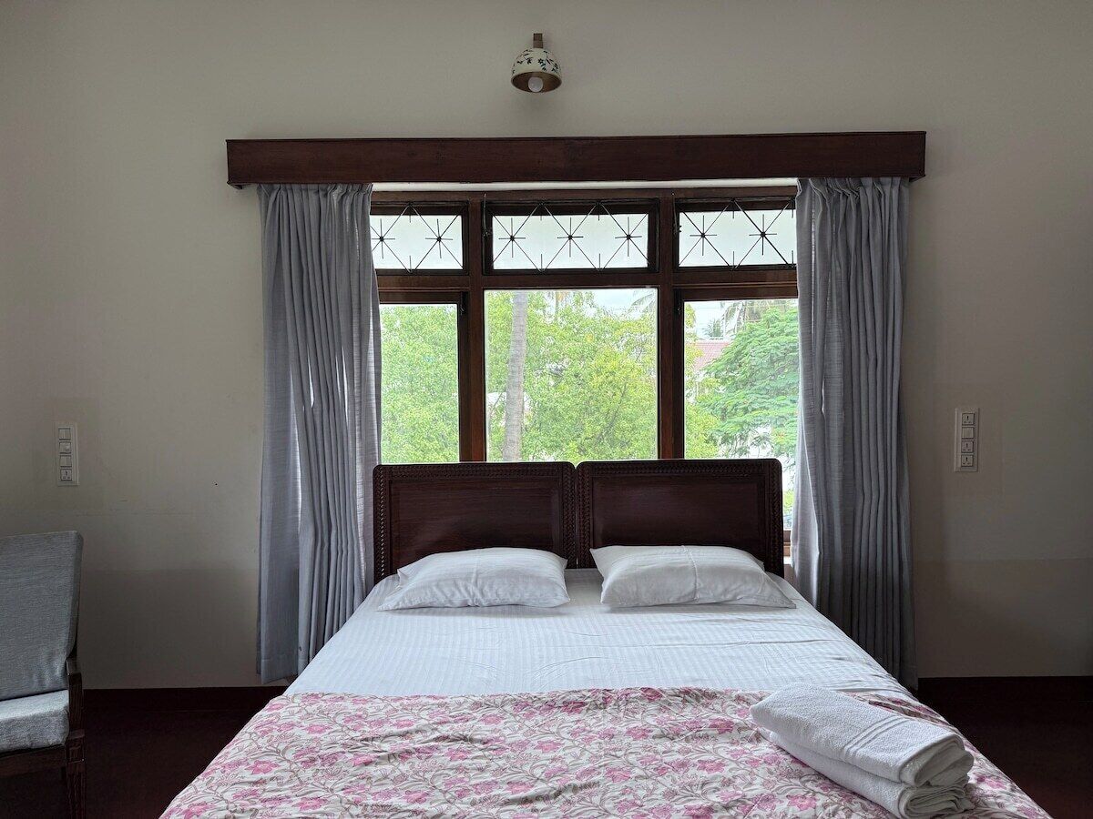 A bedroom with a bed, curtains, a chair, and a window with a view of trees.