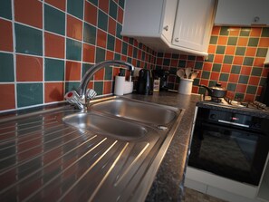 A kitchen with a stainless steel sink, a stove, and a tiled backsplash. - Woolacombe Apartment with Panoramic Sea Views (Woolacombe)