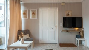 Una sala de estar con un sofá, una mesa de centro con un jarrón, un televisor sobre un mueble bajo y una puerta.