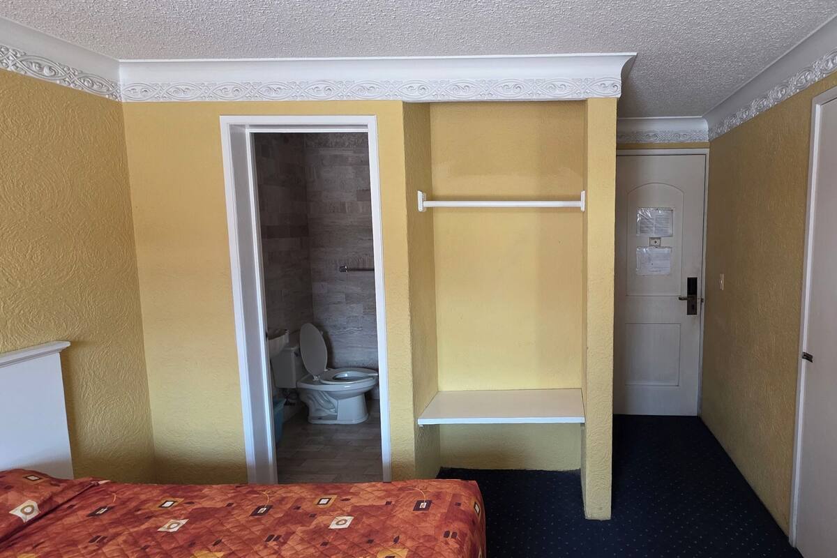 Une chambre d’hôtel comprenant un lit, une salle de bain avec des toilettes et une douche, et une porte donnant sur une autre pièce.