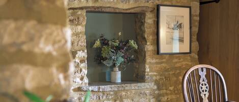 Pared de piedra con una ventana, un cuadro enmarco y una silla de madera.
