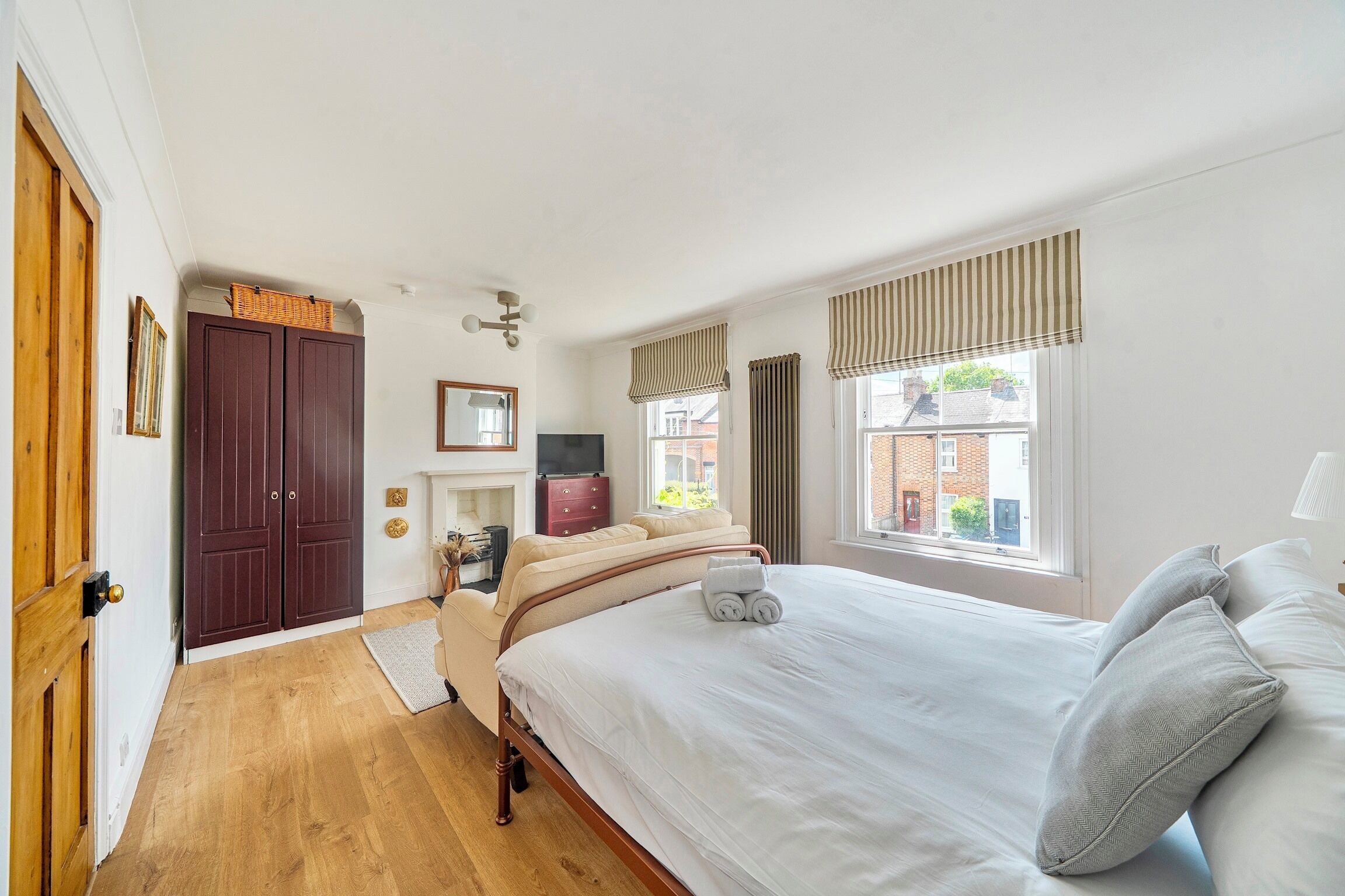 Ein Schlafzimmer mit Holzboden, einem Bett mit weißer Bettwäsche, einem Schminktisch, einem Spiegel und einem Fenster mit Vorhängen.